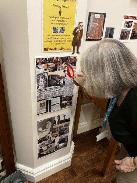 Lady with bobbed short grey hair looks through a magnifying glass at a picture.